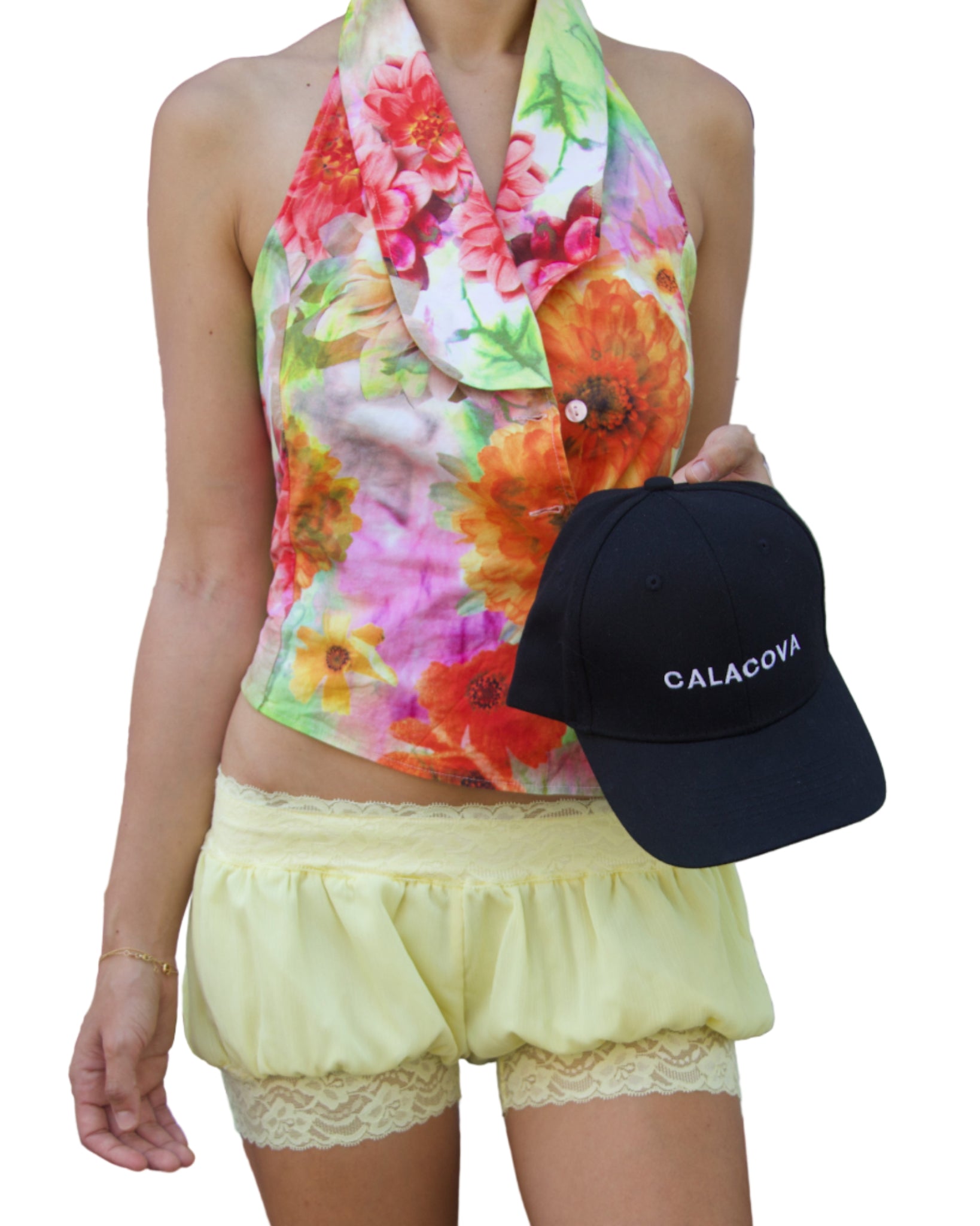 Person wearing a colorful floral top and yellow shorts, holding a black cap with 'CALACOYA' branding.