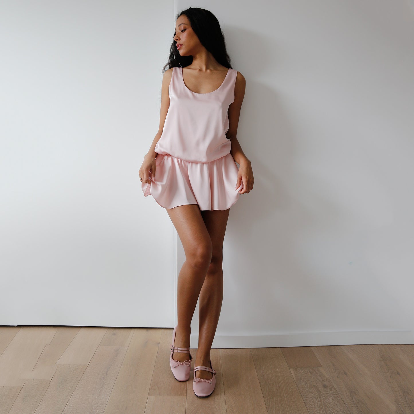Woman wearing a pink pajama set against a white wall.