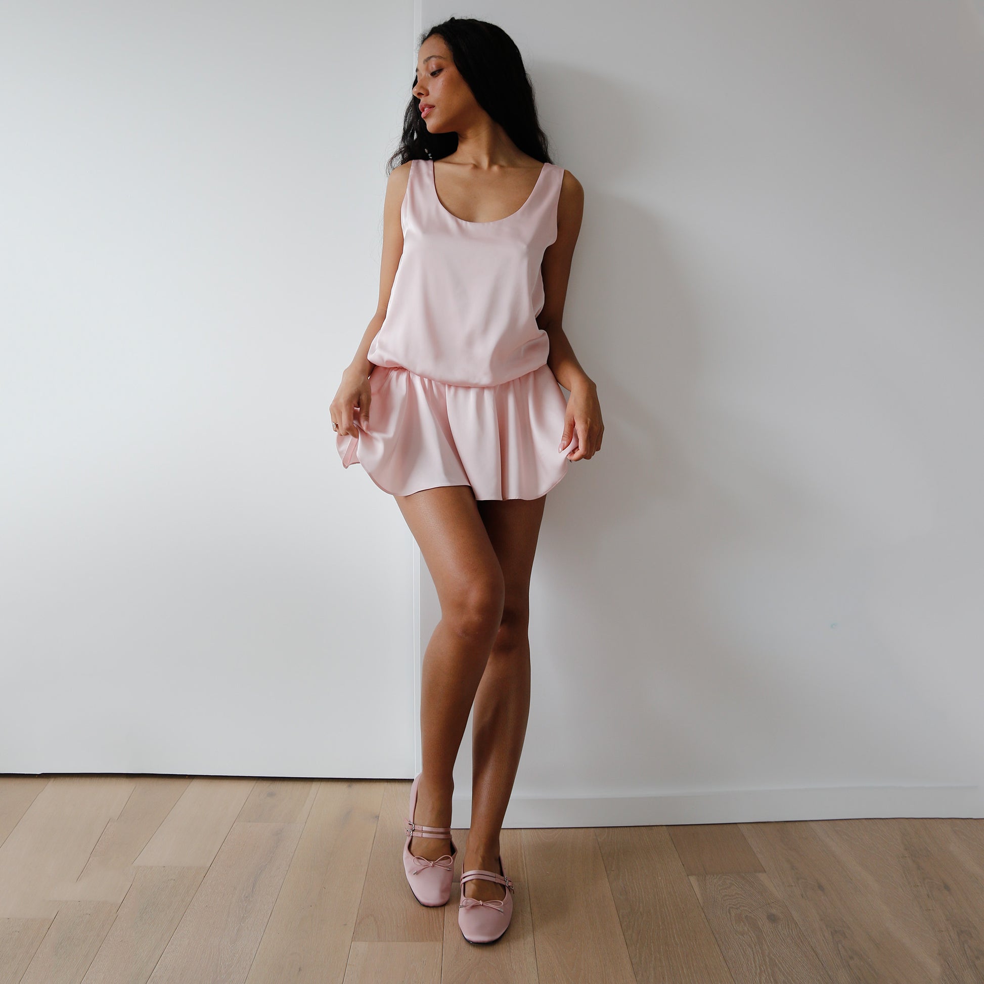 Woman wearing a pink pajama set against a white wall.