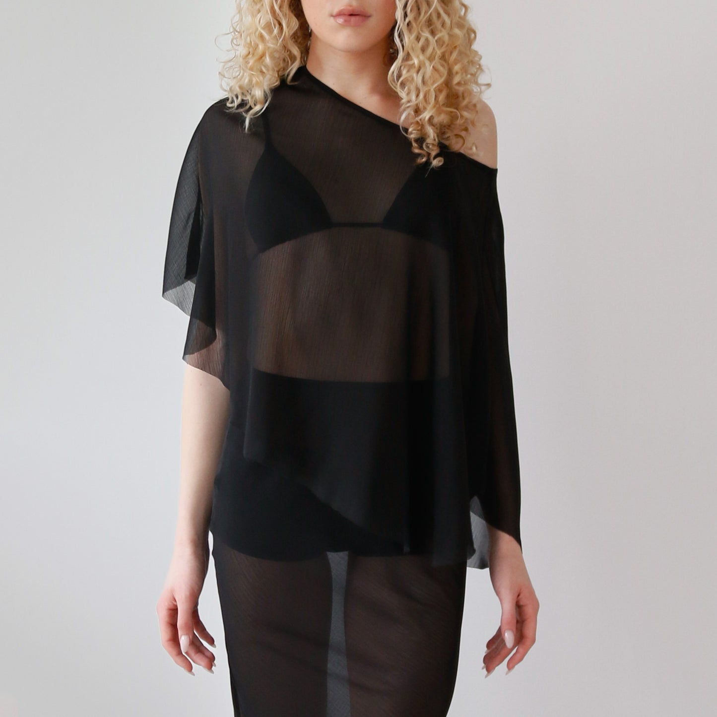 Woman wearing a black sheer top and dark pants on a plain background