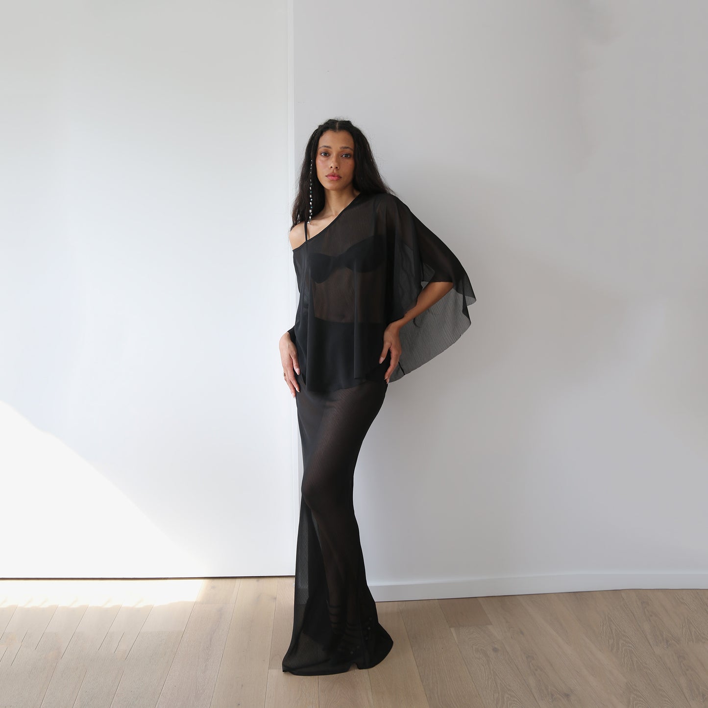 Woman wearing a black sheer set against a white wall.